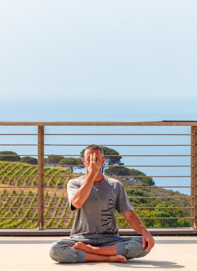 Uomo medita all'aperto con vista sul mare e vigneti.