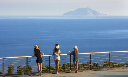 Three women gaze at the sea and distant island, enveloped in peace and beauty.