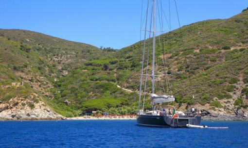 Sailboat on blue sea, secluded beach, green hills. Peace and adventure.