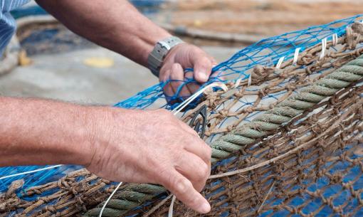 Skilled hands mend a fishing net, weaving threads with care and dedication.