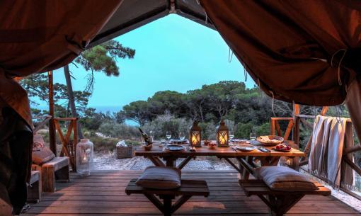 Cena romantica in tenda, natura e lanterne accese, atmosfera serena.