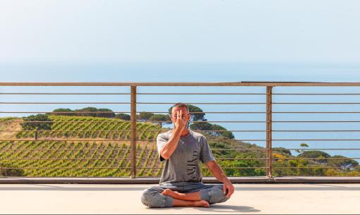 Mann meditiert im Freien mit Blick auf Meer und Weinberge.